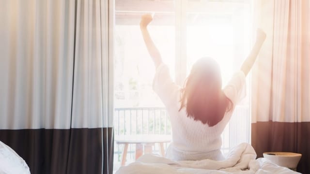 朝日を浴びてベッドで目覚める女性