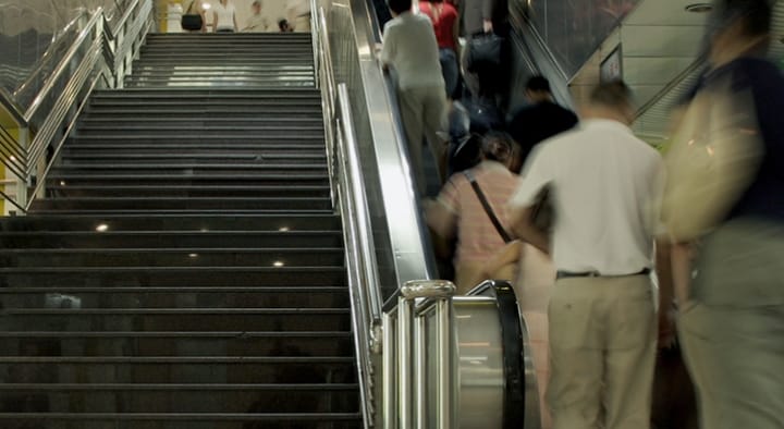 階段よりエスカレーターを利用する人々の様子